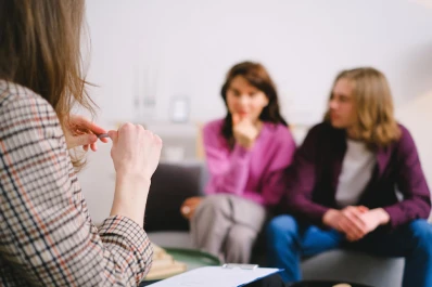 A woman facilitates a discussion with a couple in a living room, highlighting couples therapy and counseling in Singapore.
