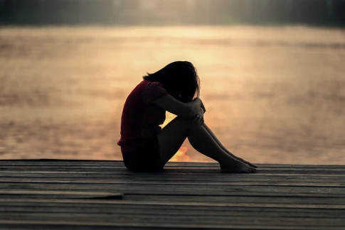 A woman sits on a dock by the water, reflecting during a serene sunset, symbolizing peace in depression therapy.