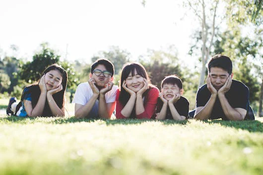A family relaxing on the grass in a park, enjoying quality time together, symbolizing family therapy in Singapore.